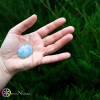 Una Calcite azzurra Burattato Lens al centro della mano immersa nel verde energetico della natura. Per scaricare lo stress e ricentrarsi nella pace interiore.